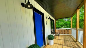 Una terraza cubierta de madera con una puerta azul, barandillas blancas y dos macetas.