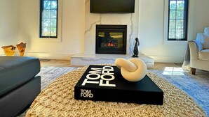Una sala moderna con chimenea, un televisor de pantalla plana montado encima y un libro titulado "Tom Ford" sobre una alfombra.
