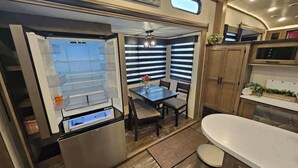A compact kitchen with a refrigerator, a dining table, and a bar area. - RV8 | Family Beach Getaway - Luxury Sabre (Bolivar Peninsula)