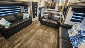 A compact living space with a sofa, a smaller couch, and a bed. - RV8 | Family Beach Getaway - Luxury Sabre (Bolivar Peninsula)