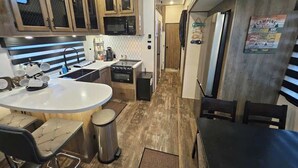 A compact kitchen with a microwave, stove, and sink. There is a dining area with a table and chairs. - RV8 | Family Beach Getaway - Luxury Sabre (Bolivar Peninsula)