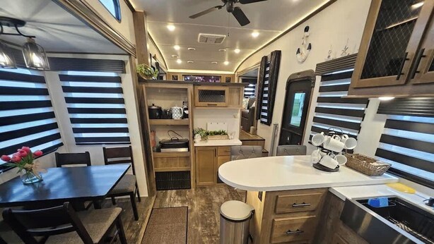 A compact kitchen with a dining area, wooden cabinets, a small trash bin, and a ceiling fan. - RV8 | Family Beach Getaway - Luxury Sabre (Bolivar Peninsula)