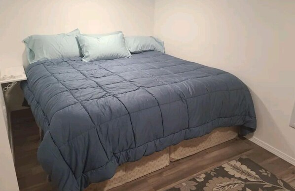 A neatly made bed with a blue quilt and two pillows, a wooden floor, and a small rug. - Private basement studio apt.
(Spokane)