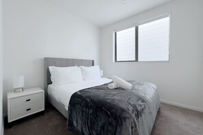 Un dormitorio con cama, mesita de noche, ventana y piso alfombrado.