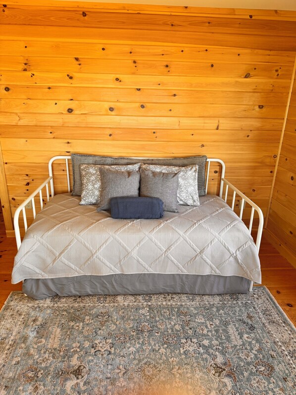 A bed with a quilted headboard, a patterned rug, and a wooden wall.