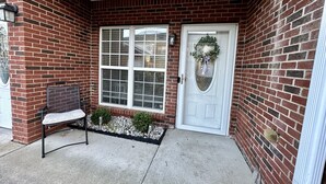 Une façade en briques avec une porte blanche, un banc et un petit espace aménagé en jardin.