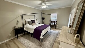Une chambre à coucher avec un lit à baldaquin, un ventilateur de plafond, une fenêtre avec des stores, une commode et un miroir.