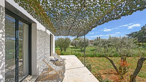 A modern outdoor seating area with a pergola providing shade, a stone patio, and a view of an olive grove. - Nice home in Saint-Maximin (Saint-Maximin)
