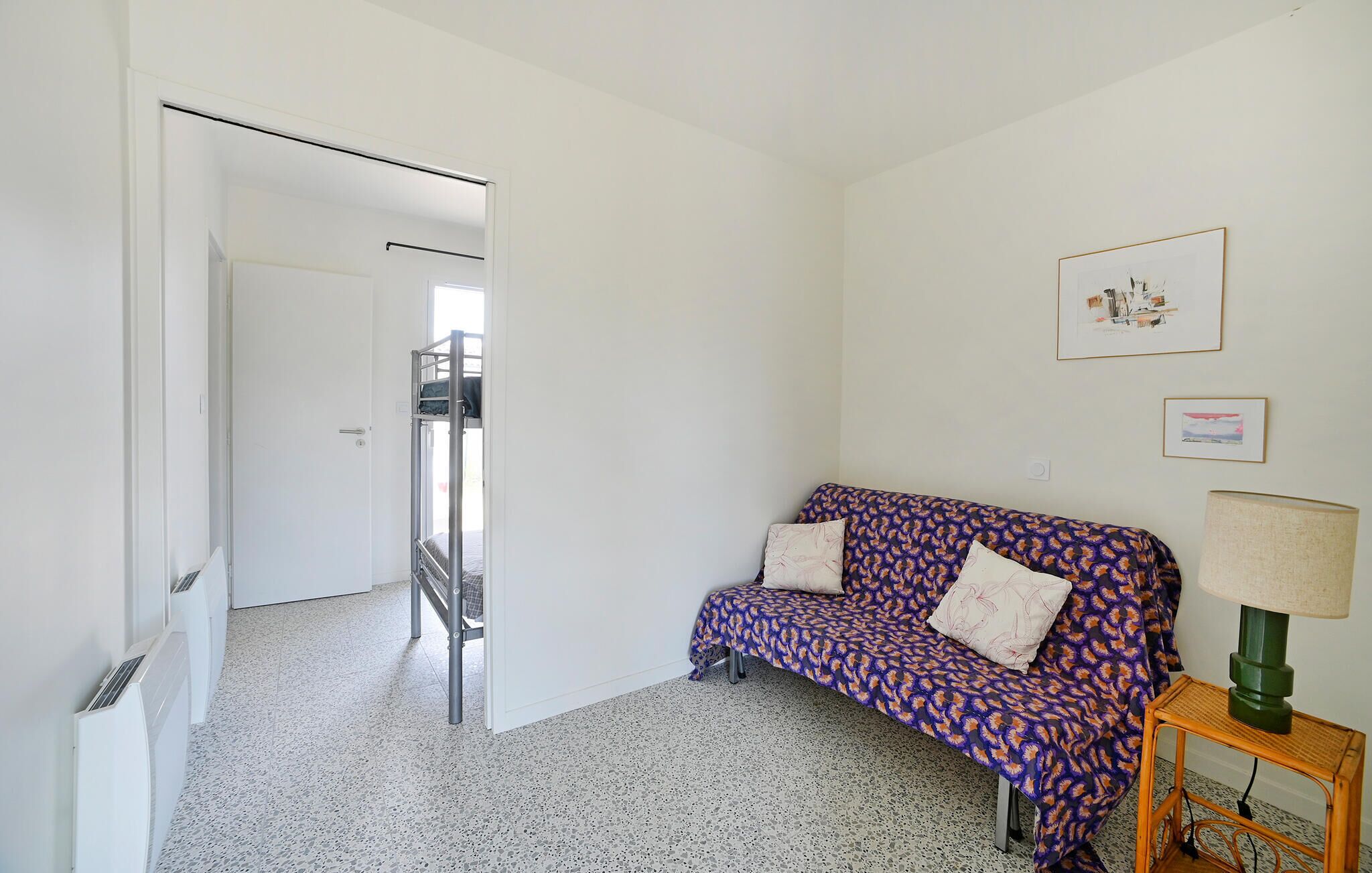 A room with a bunk bed, a patterned sofa, a lamp, and framed pictures on the wall.