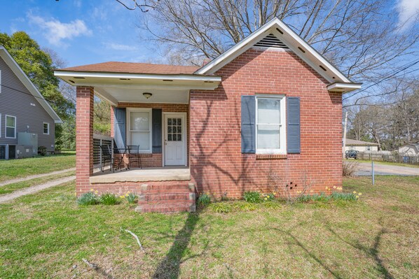 A single-story brick house with a front porch, a door, and a window with shutters.