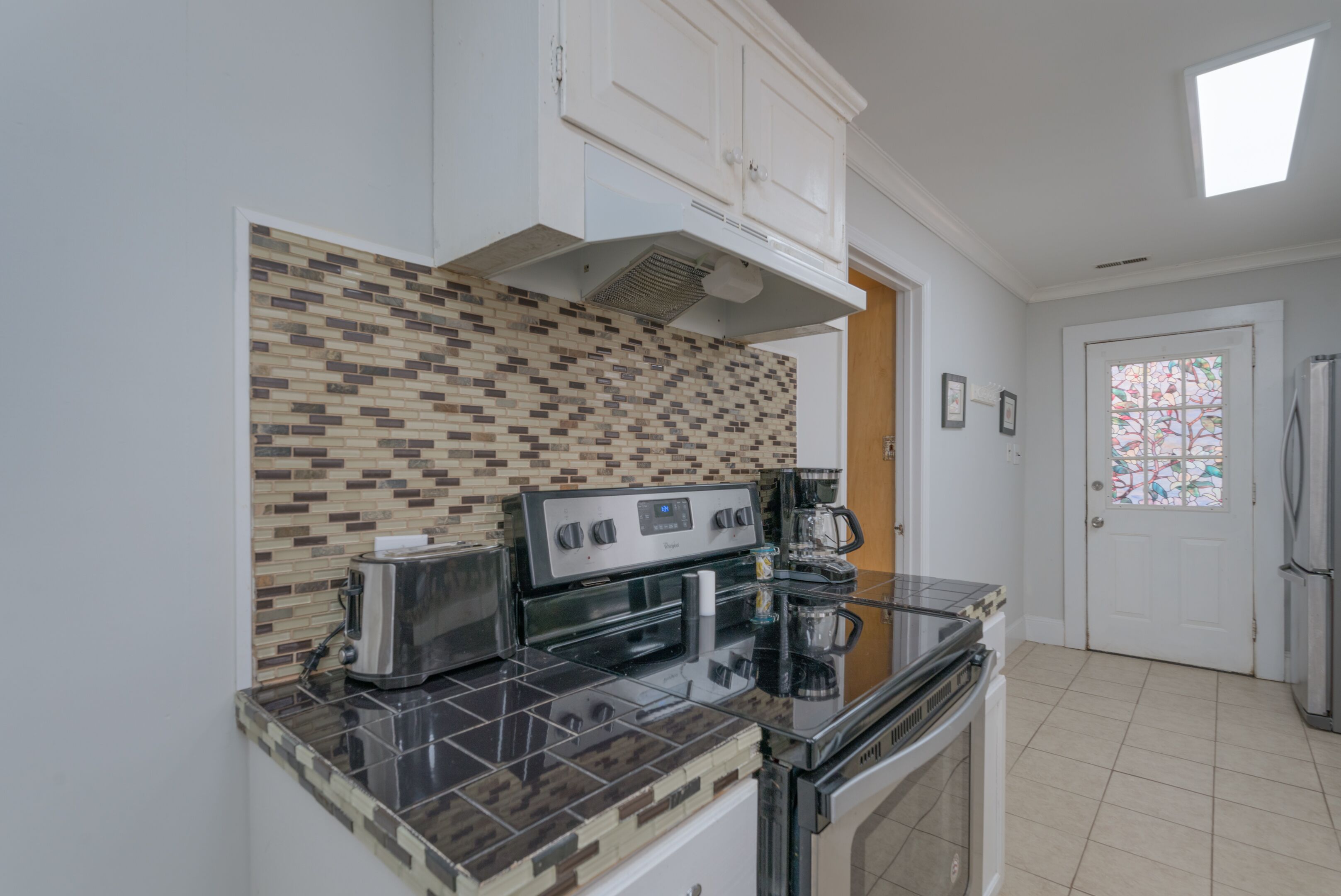 A kitchen with a tiled backsplash, a stove, a toaster, and a refrigerator.