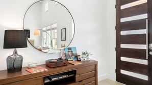 A room with a wooden dresser, a round mirror, a lamp, and a door with horizontal slats. - Willie's Haus | 2/2, Full Kitchen, Hot Tub, Washer/Dryer, King Beds, Great Location (Fredericksburg)