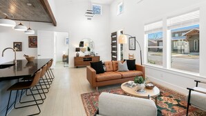 A modern living room with a brown leather sofa, a round coffee table, and a dining area with a black countertop and metal chairs. - Willie's Haus | 2/2, Full Kitchen, Hot Tub, Washer/Dryer, King Beds, Great Location (Fredericksburg)