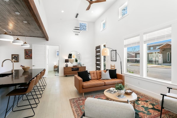 A modern living room with a brown leather sofa, a round coffee table, and a dining area with a black countertop and metal chairs.