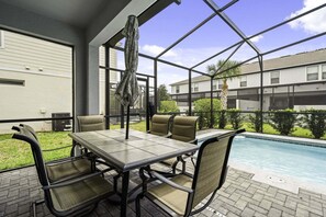 Um pátio externo com piscina, uma mesa e cadeiras, e vista para um edifício ao fundo.