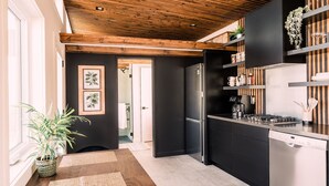 Une cuisine moderne avec un plafond en bois, des meubles de couleur noire, des appareils en acier inoxydable et un coin repas comprenant une table et une plante.