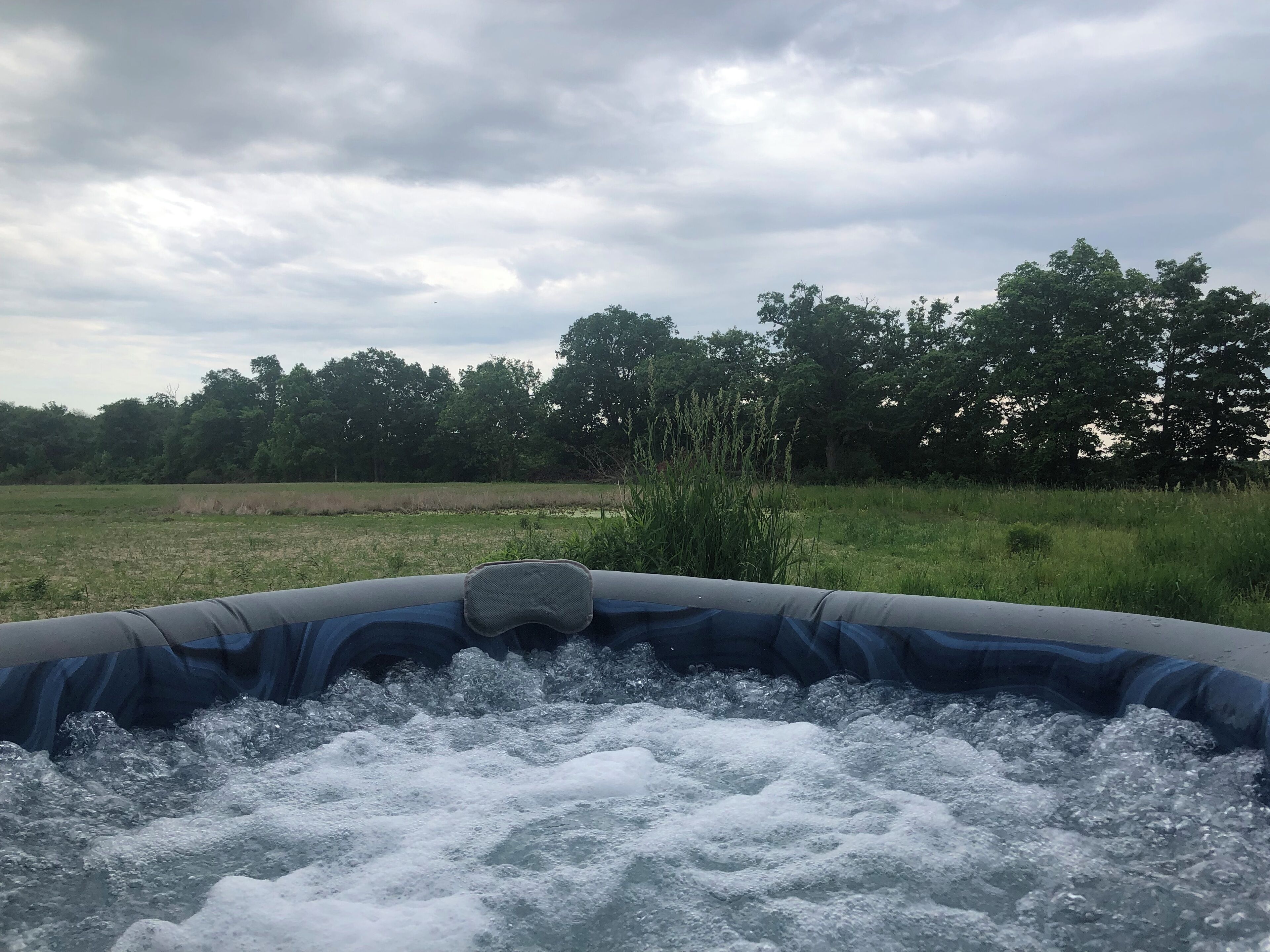 An inflatable hot tub with a view of a grassy field and trees in the background.