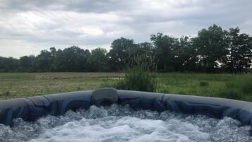 An inflatable hot tub with a view of a grassy field and trees in the background.