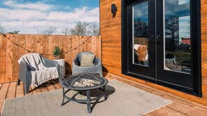 Une terrasse en bois avec des meubles d’extérieur, un foyer et une porte-fenêtre coulissante donnant sur une pièce.