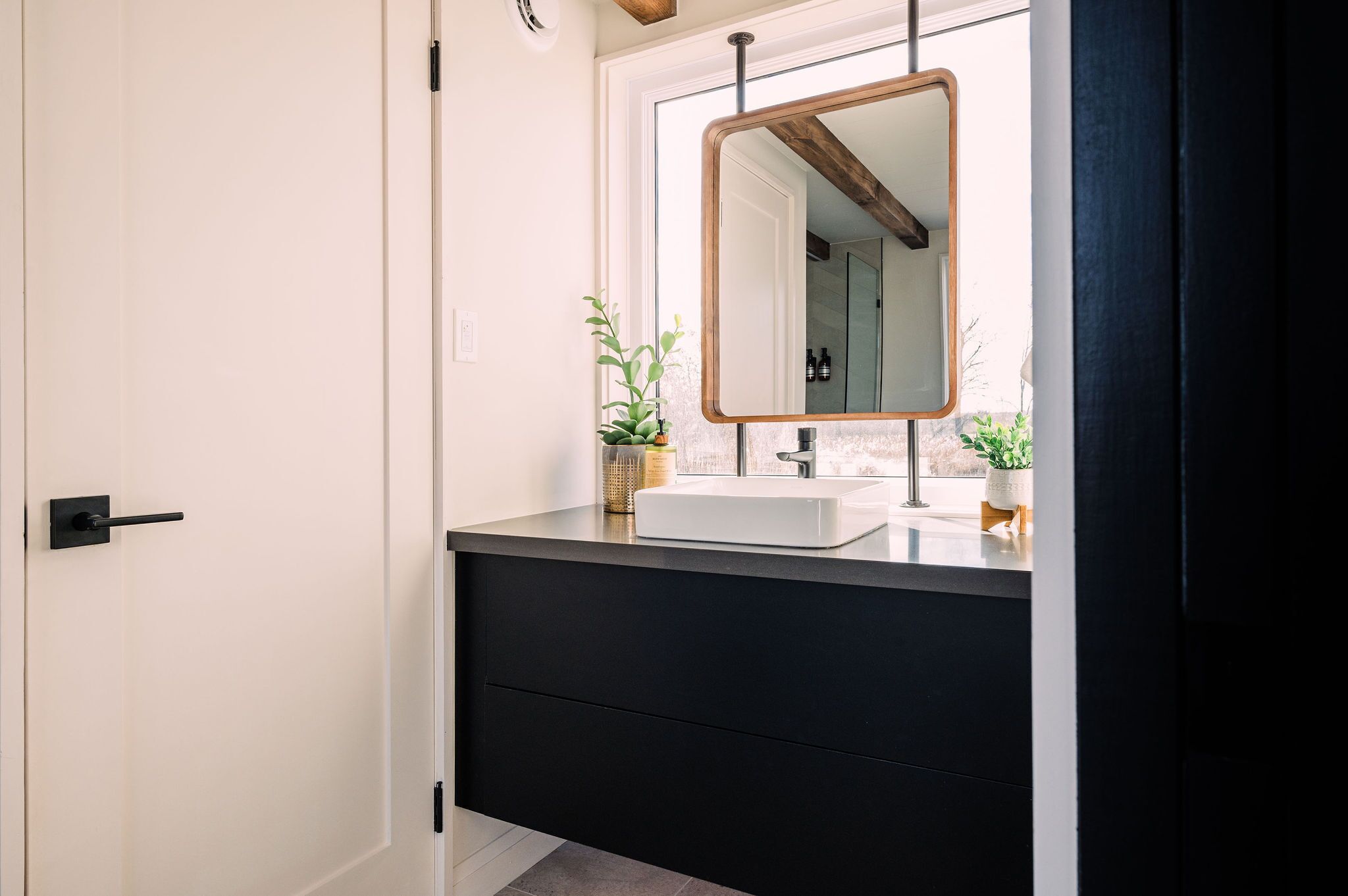A modern bathroom with a black vanity, a white sink, and a large mirror.