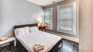 A neatly made bed with white linens, a bedside lamp, and a small wooden nightstand. - Norfolk Apartment: 1 Mi to Ocean View Beach Park! (Norfolk)