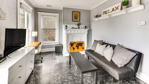 A modern living room with a sofa, a bench, a TV, a fireplace, and a world map artwork. - Norfolk Apartment: 1 Mi to Ocean View Beach Park! (Norfolk)
