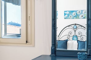 Una stanza con una finestra, un letto con testiera, un quadro e un vaso azzurro.