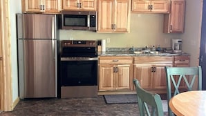 A kitchen with wooden cabinets, stainless steel appliances, and a dining area with a table and chairs. - Cabin 2 at Timberlane Resort on Long Lake (Park Rapids, MN)