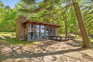 A stone cabin with large windows, a wooden deck, and a forested backdrop.