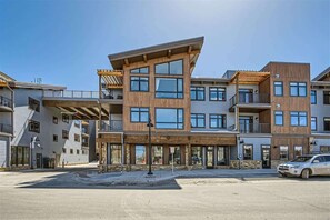 A multi-story building with a modern architectural design, featuring balconies, large windows, and a mix of wood and stone materials.