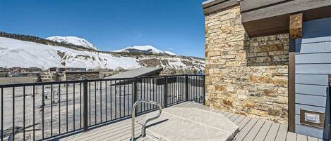 A balcony with a stone wall, a metal railing, and a view of snow-covered mountains.