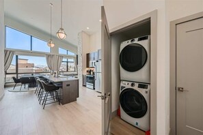 A modern kitchen with a dining area, large windows, and a built-in washer and dryer.