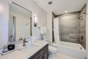 Un baño moderno con un espejo grande, un lavamanos, un inodoro y una ducha a ras de suelo.