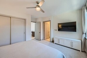 A bedroom with a bed, a ceiling fan, a TV, and a walk-in closet.