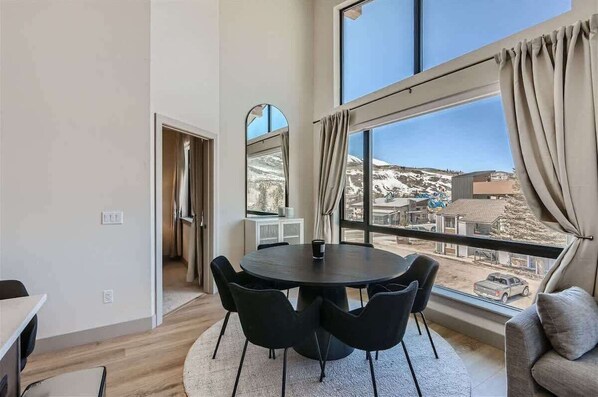 Una habitación moderna con un ventanal grande, una mesa redonda con sillas y vistas a un paisaje nevado.