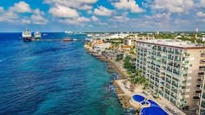 A coastal hotel with a pool, ocean view, and a pier with a cruise ship.