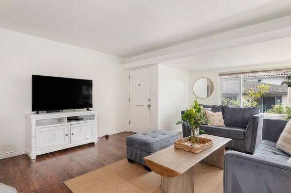 A modern living room with a flat-screen TV, grey sofa, and a wooden coffee table.