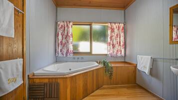 A bathroom with a wooden bathtub, a window with floral curtains, and a towel rack with a towel saying "Stay".