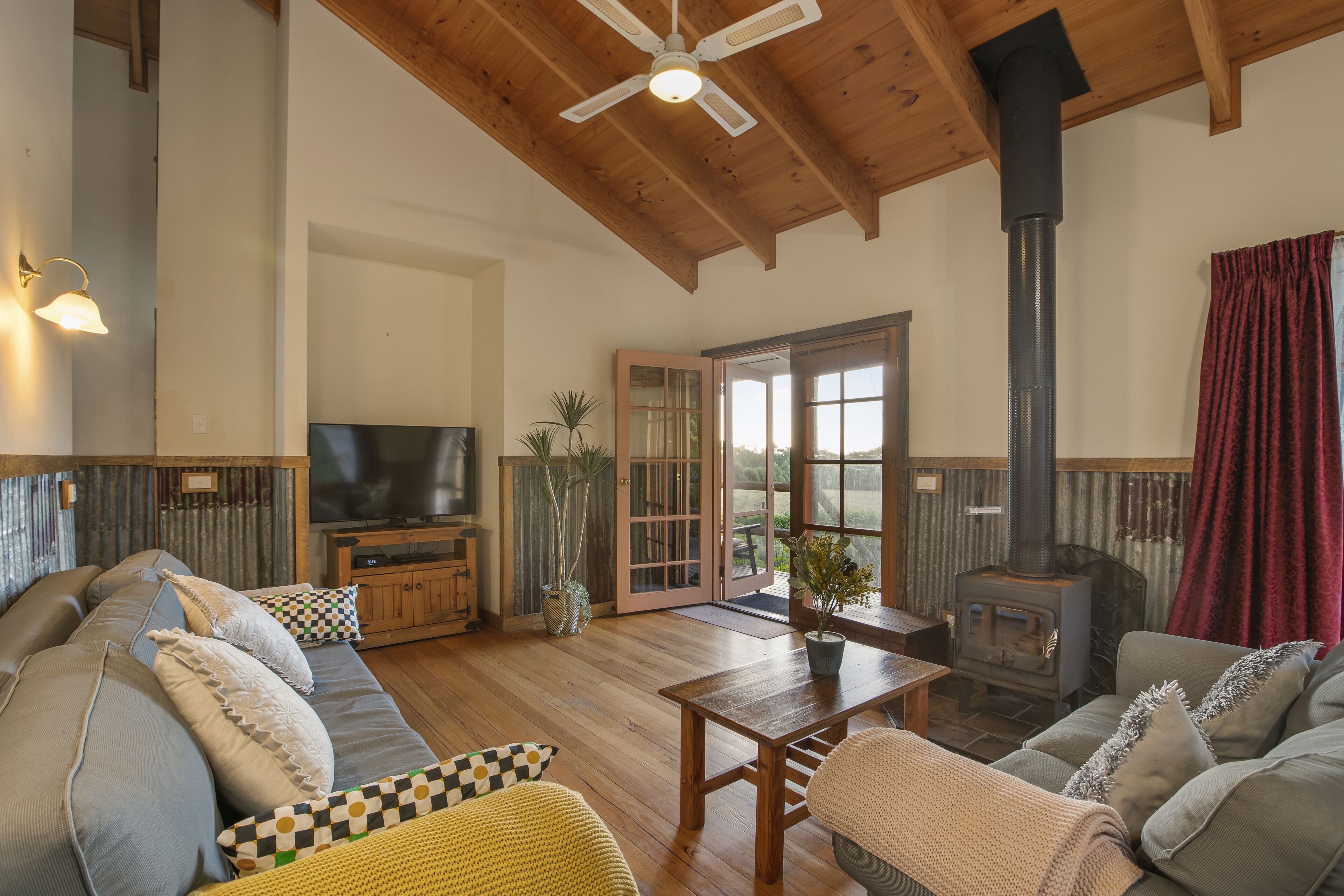 A cozy living room with a wooden ceiling, a television, a fireplace, and a sofa with cushions.