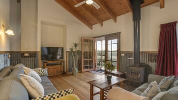 A cozy living room with a wooden ceiling, a television, a fireplace, and a sofa with cushions.