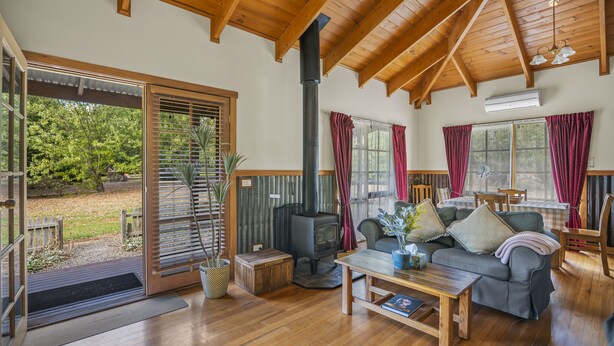 A cozy living room with a wooden ceiling, a fireplace, a sofa, a coffee table, and a dining area. - StayAU Conifer Cottage Lakeside Haven (Badger Creek)