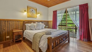 A wooden-framed bedroom with a bed, bedside table, and a window with curtains. - StayAU Conifer Cottage Lakeside Haven (Badger Creek)