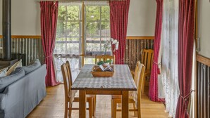 A cozy room with a wooden ceiling, a dining table with chairs, a sofa, and a large window with curtains. - StayAU Conifer Cottage Lakeside Haven (Badger Creek)