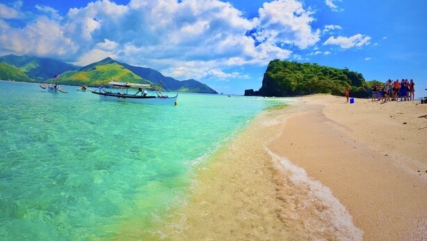 A beach with clear turquoise water, a sandy shore, and a boat in the water.