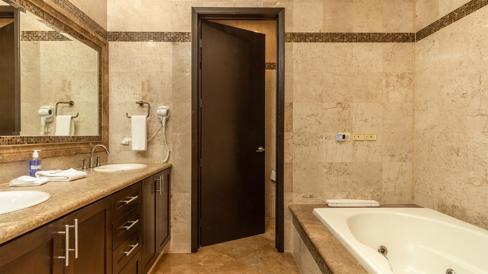 A bathroom with a double sink vanity, a large mirror, a hairdryer, and a bathtub.