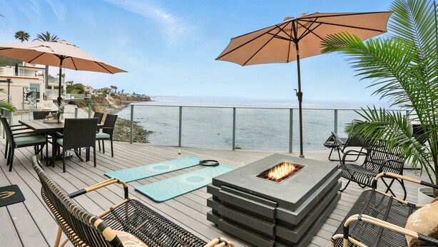 A deck with outdoor furniture, a fire pit, and umbrellas overlooking the ocean. - Luxury, renovated, oceanfront home with incredible deck & ocean views - dog friendly! (La Jolla)