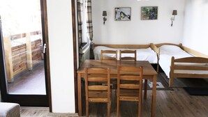 A cozy room with a wooden table and chairs, a sofa, and a bed. There are two wall-mounted lamps and two framed pictures.