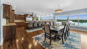 A spacious kitchen with wooden cabinets and a large island, a dining area with a view of the water, and a modern chandelier.
