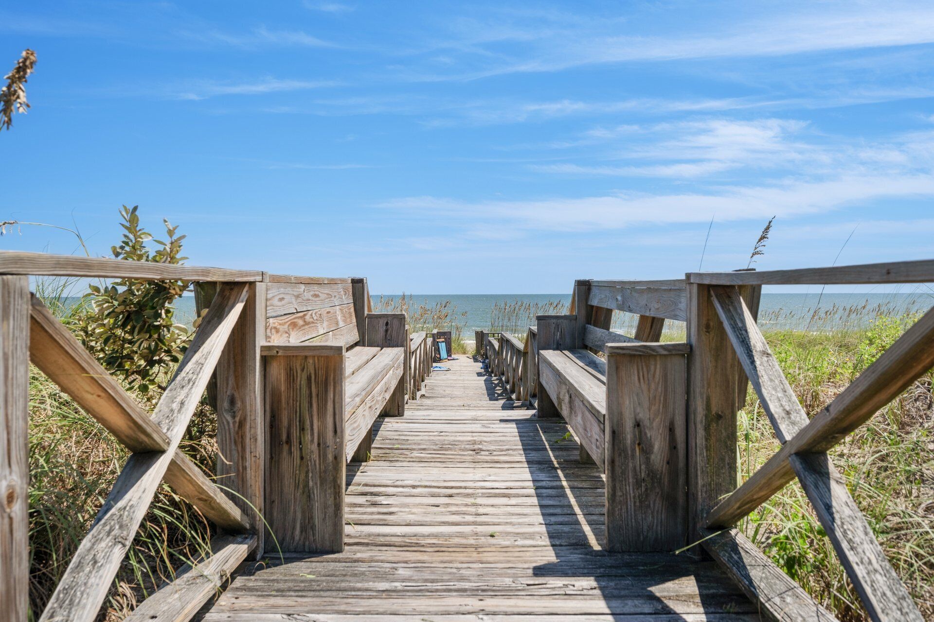 Ein Holzsteg führt zu einem Strand mit freiem Blick auf das Meer.