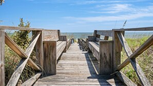 Une promenade en bois qui mène à une plage offrant une vue dégagée sur l’océan.